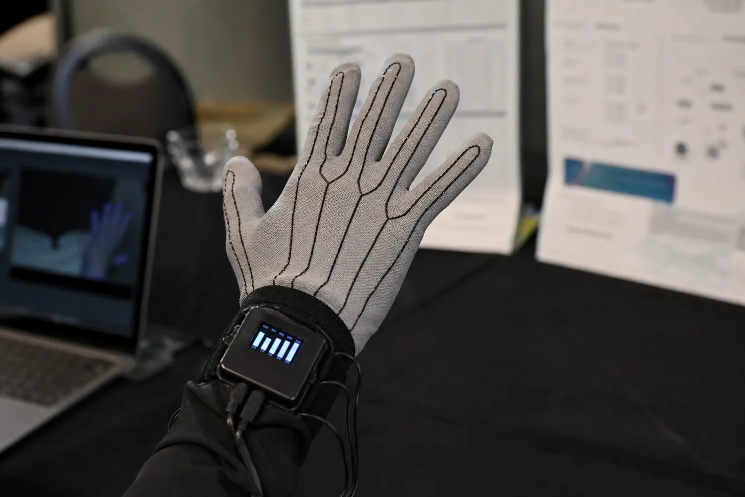 Demo glove with printed finger traces and a small wrist module with a screen, on a conference table